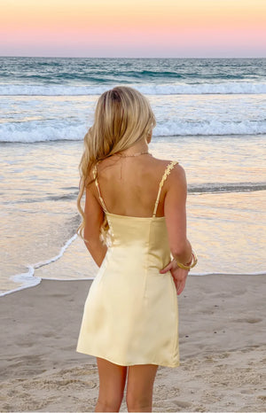 Rear view of a yellow satin mini dress with a straight back and delicate flower details on the spaghetti straps