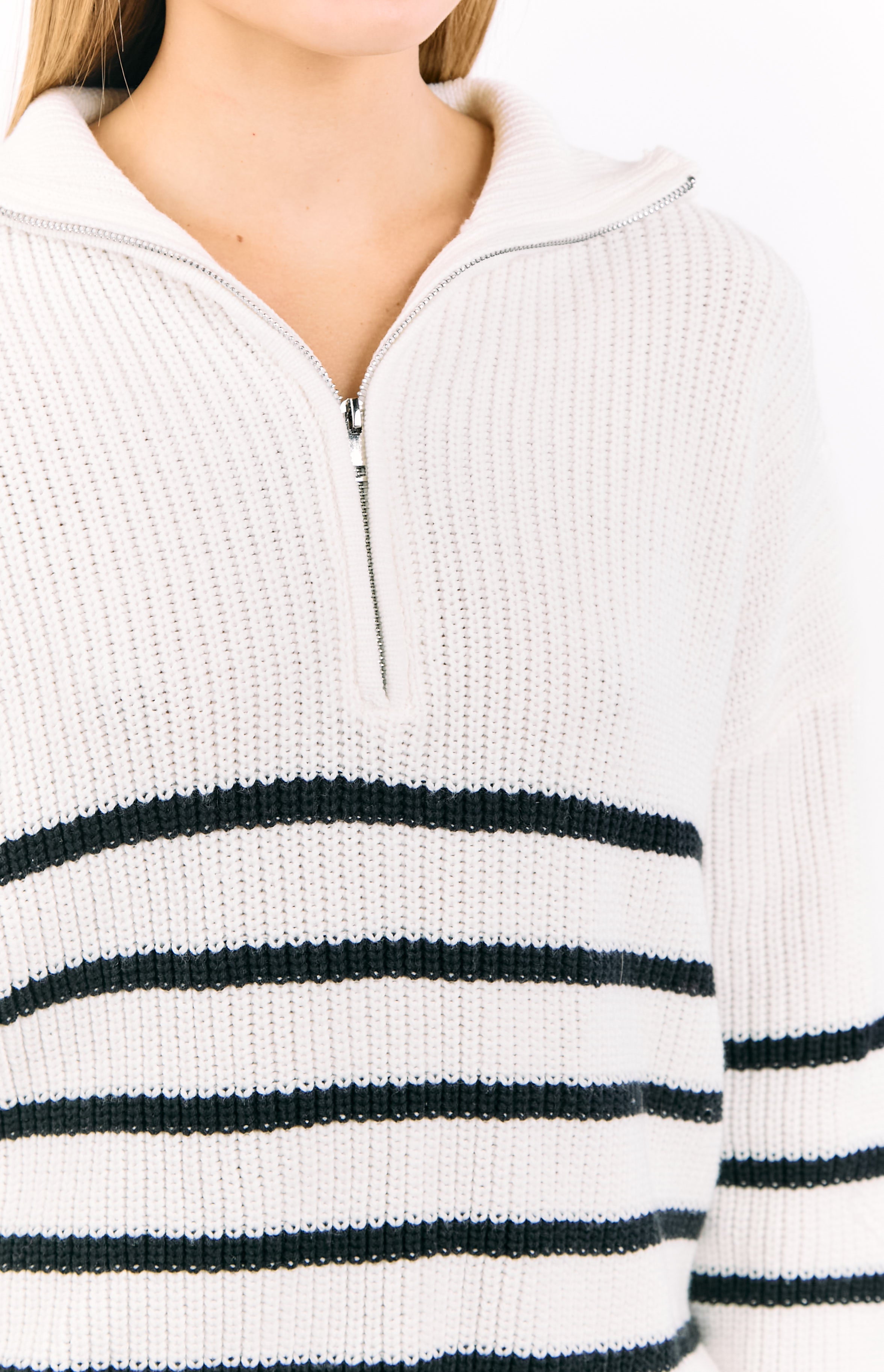 Close-up of the cream knit fabric with black stripes and silver quarter zip detail