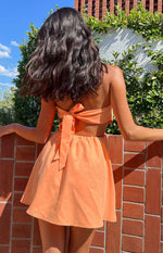 Back view of an orange strapless mini dress with a tie-back closure and waist cutout