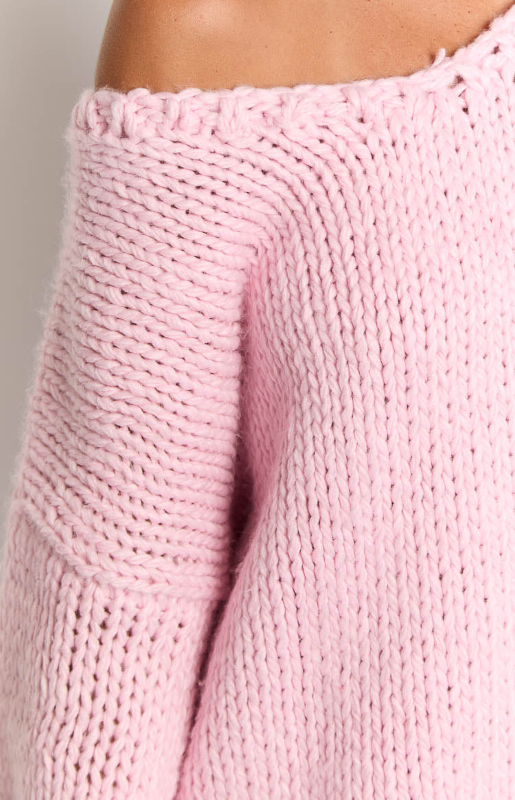 Close-up of a light pink chunky knit sweater showing the wide V-neck with open knit detail and voluminous sleeves