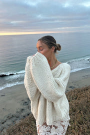 Cream chunky knit sweater with an oversized fit, wide V-neck, and long, voluminous sleeves