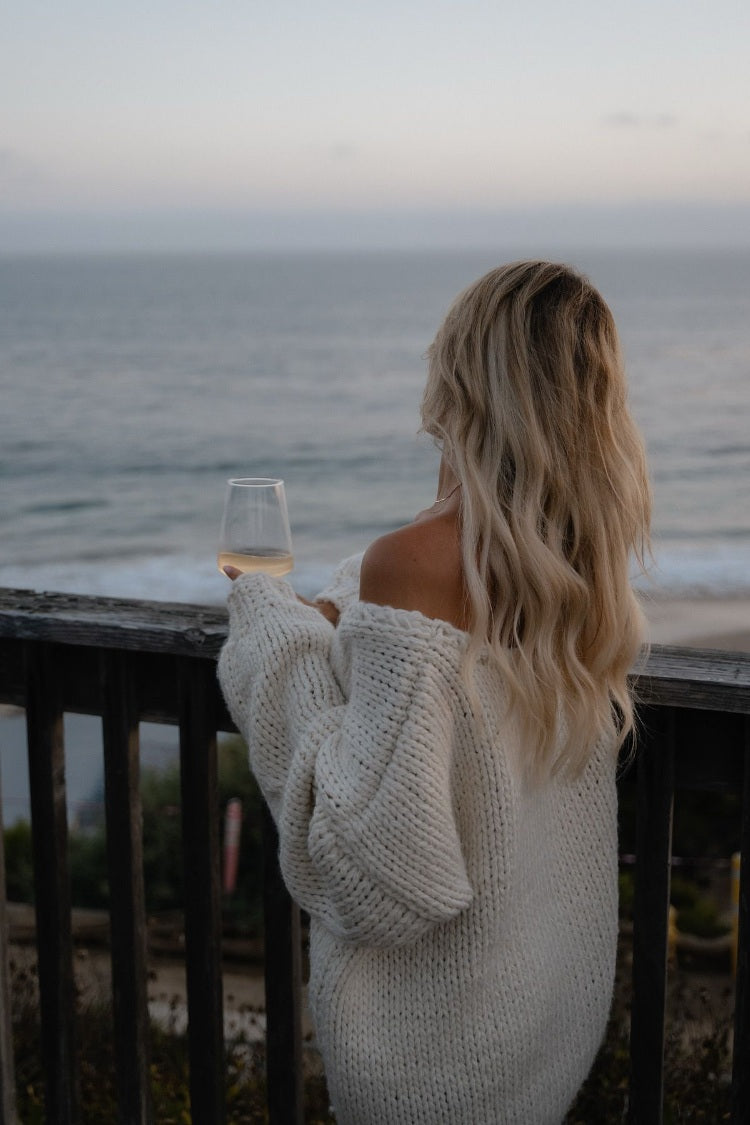 Side view of a cream chunky knit sweater with an off-shoulder neckline and voluminous long sleeves