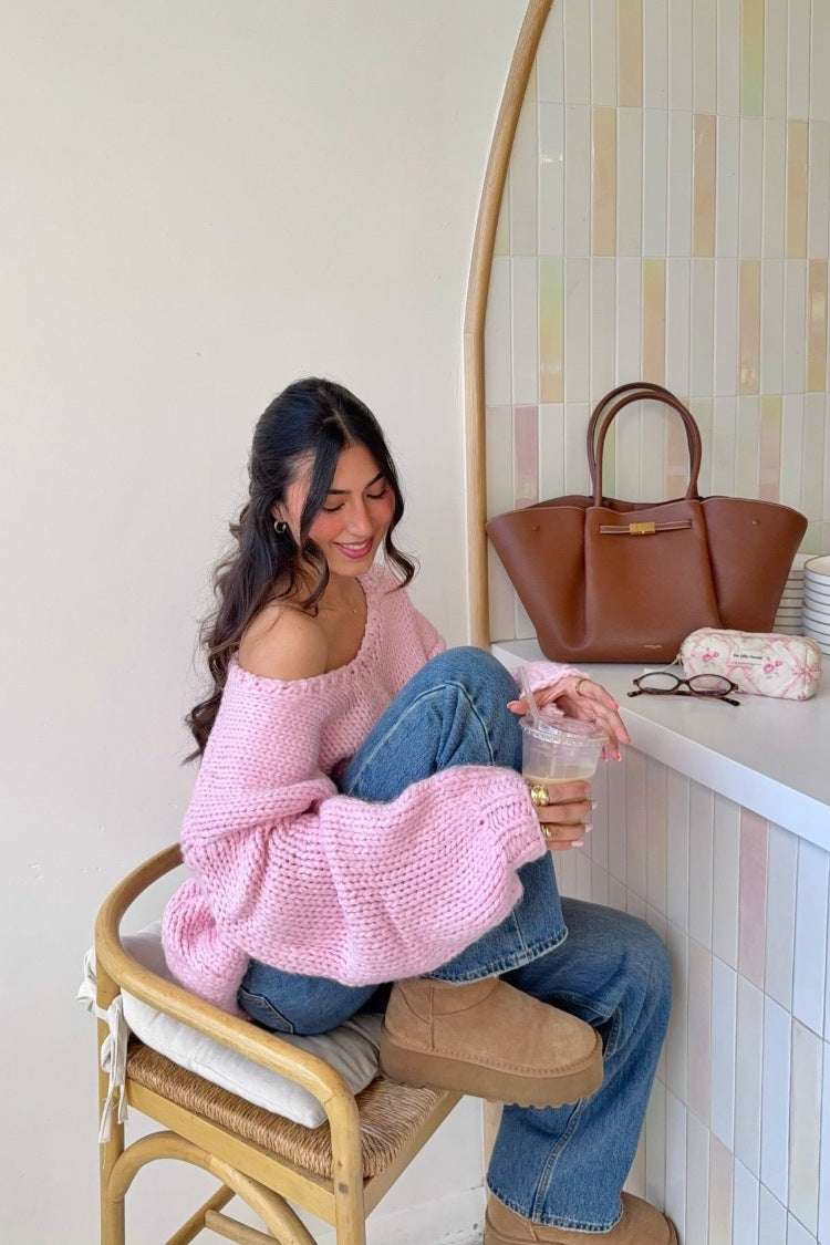 Side view of a light pink chunky knit sweater with an off-shoulder neckline and wide slouchy sleeves