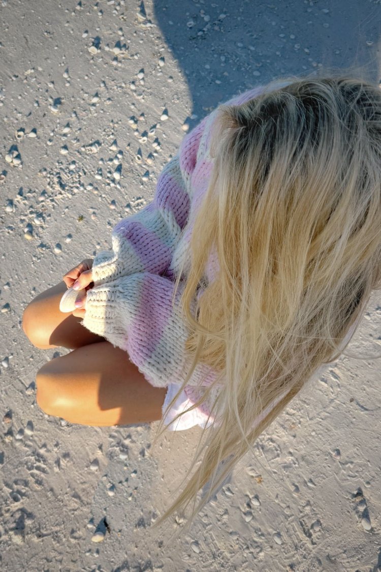 Close-up overhead of a pink, purple, and white striped chunky knit sweater with wide ribbed cuffs
