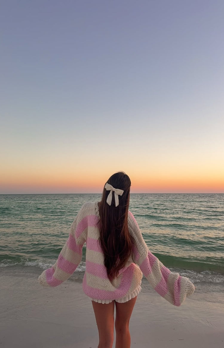Rear view of a pink and white striped chunky knit sweater with wide sleeves and ribbed cuffs