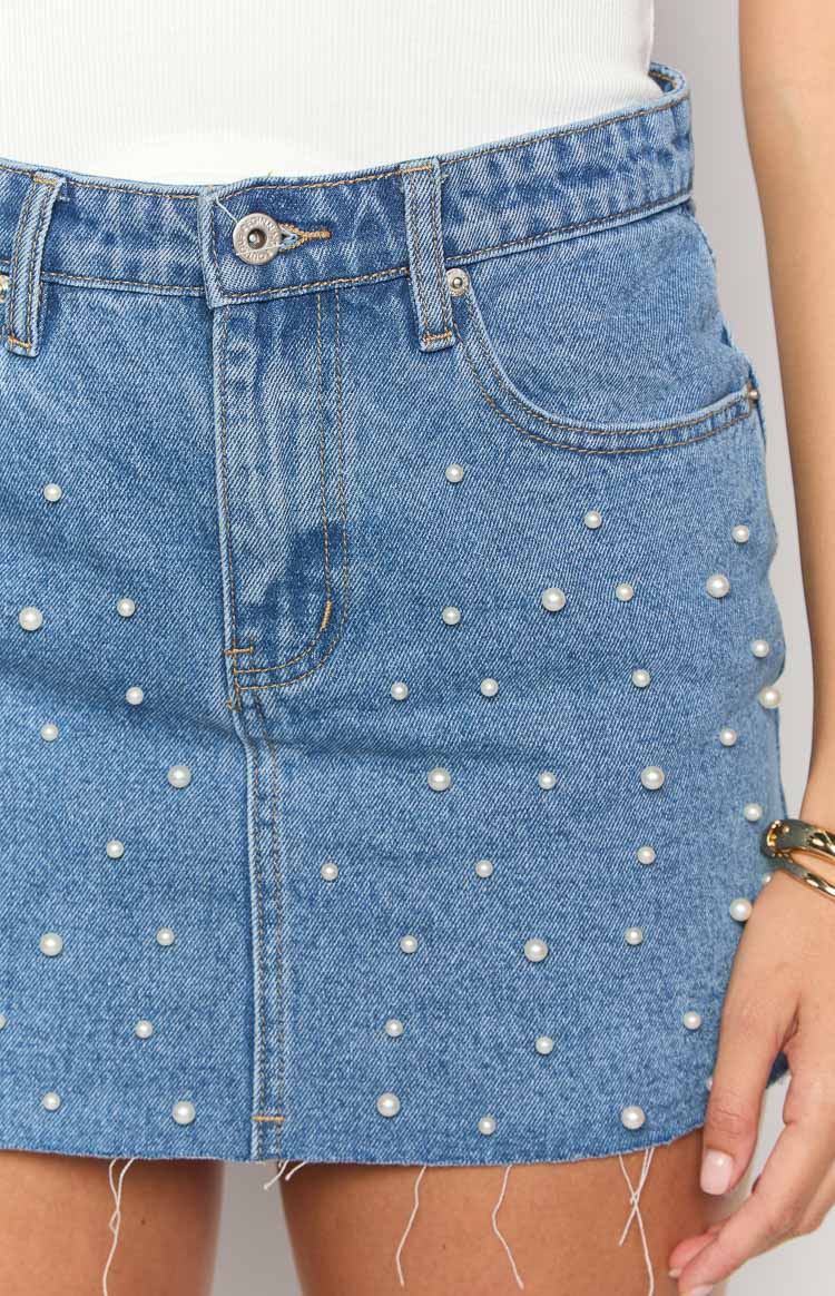 Close-up of the mid-wash denim mini skirt with scattered pearl embellishments and a frayed hem