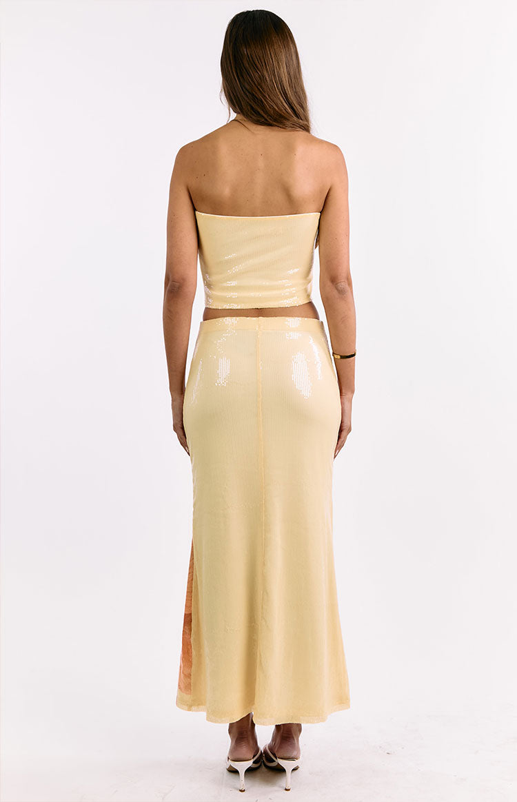 Rear view of the yellow sequin maxi skirt with a vertical seam and a side slit revealing a floral pattern