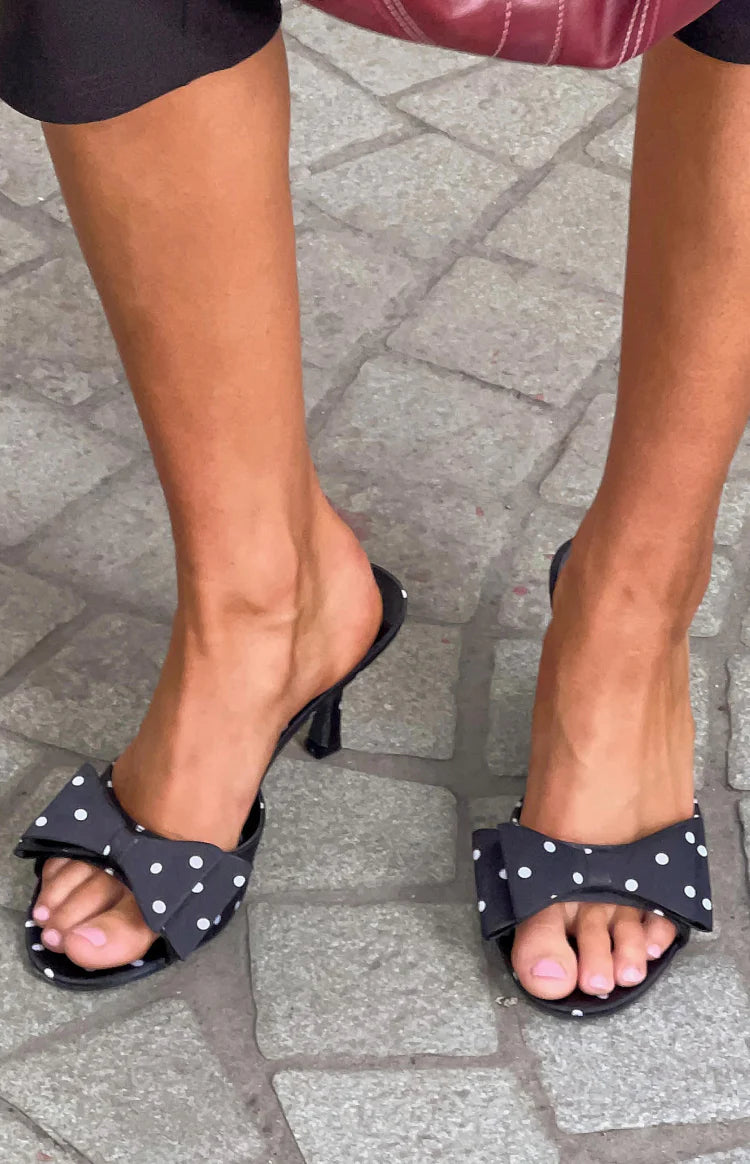 Top-down view of black polka dot heeled mules with a prominent bow on the front strap