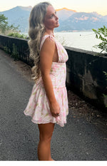Side view of a pink floral mini dress with tie-shoulder straps, deep armholes, and a ruched waist leading to a flowy tiered s