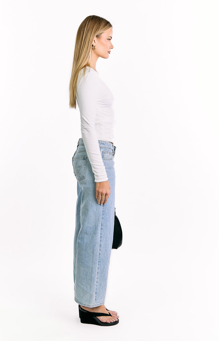 Side view of the fitted white long sleeve top, highlighting its smooth jersey fabric and simple crew neckline