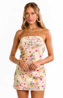 Back view of our model wearing a pale yellow mini dress with a multicolored floral pattern. The dress features a large cut-out at the back with a tie closure at the top.