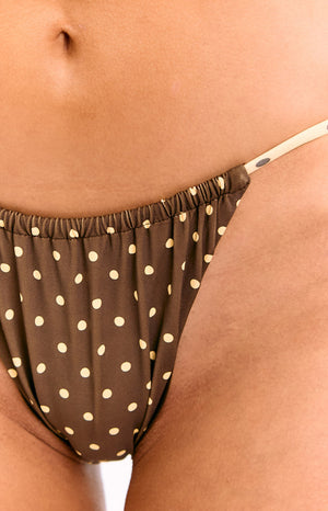 A close-up view of our model showing a pair of brown bikini bottoms with small white polka dots and a ruched gathered detail at the top. This bikini string tie is yellow with black polka dots.