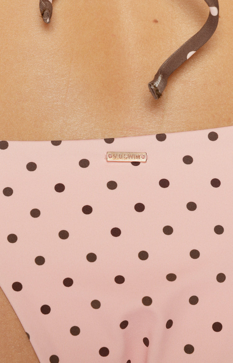 Close-up of pink polka dot bikini bottoms with a gold 9.0 SWIM metal tag and brown tie detail