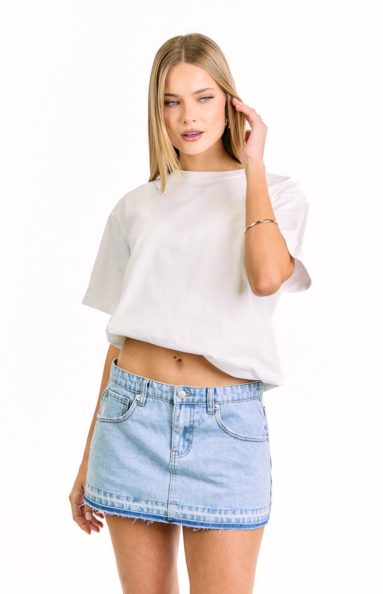 Light wash denim mini skirt with front pockets, button and zip fly, and a distressed hem with a darker band