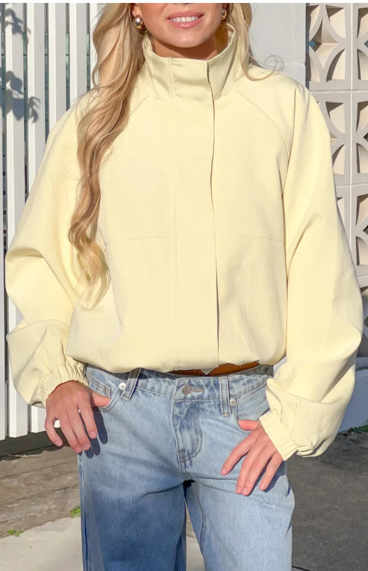 Front view of a yellow funnel neck sports jacket with a hidden placket and voluminous long sleeves with elasticated cuffs