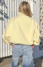 Rear view of a yellow funnel neck sports jacket with raglan sleeves and an elasticated hem