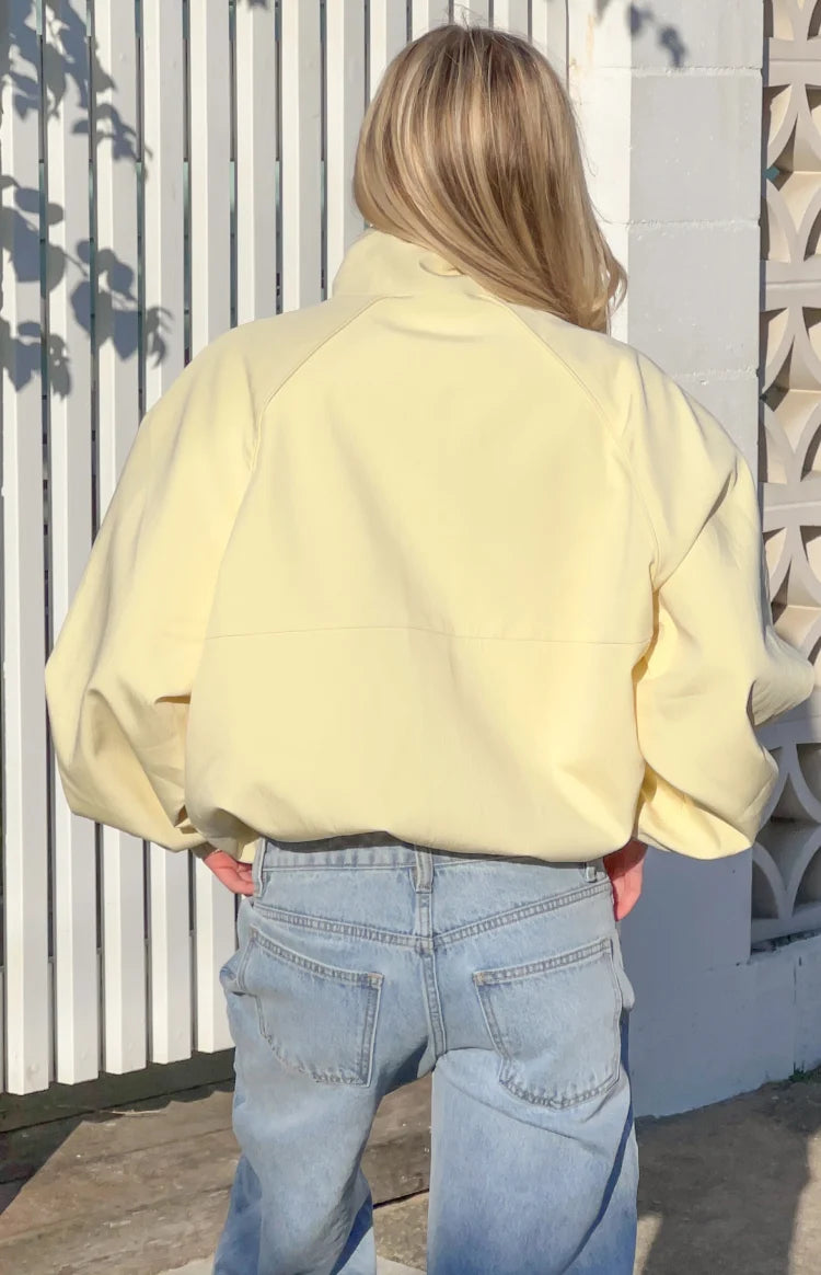 Rear view of a yellow funnel neck sports jacket with raglan sleeves and an elasticated hem