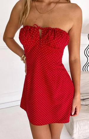 Fashion model showcasing a playful red and white polka dot strapless mini dress with a ruffled neckline and charming front tie- perfect for a casual or festive occasion.