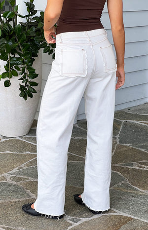 Rear view of white denim jeans with scallop edge back pockets, contrast stitching, and raw hems