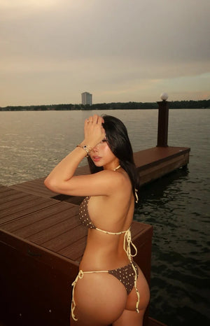 Side and rear view of brown polka dot bikini bottoms with yellow tie sides and a cheeky fit