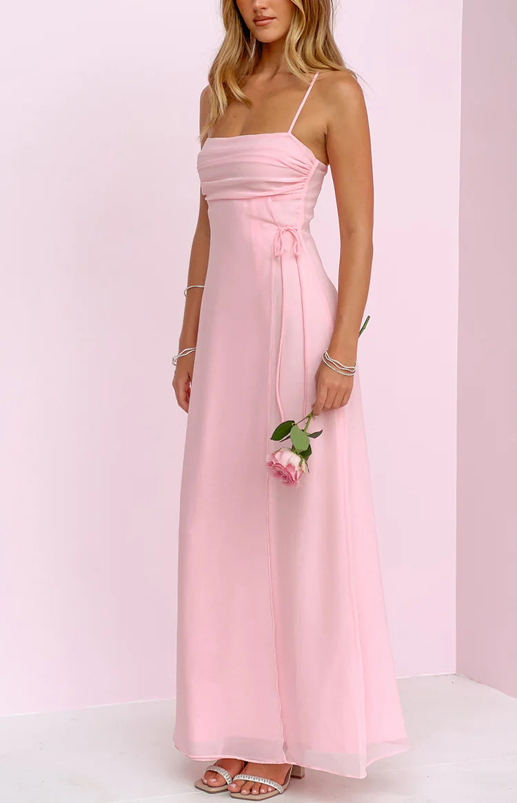 Rear-side view of a pink maxi dress showing thin spaghetti straps, a low back, invisible zipper, and side ruching