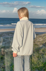 Rear view of a blue stripe mock neck sweater with a cream collar, relaxed fit, and ribbed cuffs and hem
