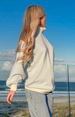 Side view of a blue and white striped mock neck sweater with long balloon sleeves and cream ribbed cuffs and hem