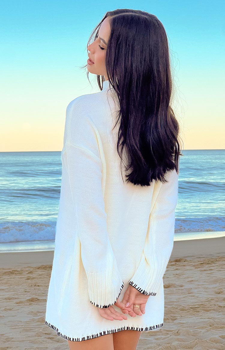 Rear view of a cream knit sweater dress with black contrast trim on the cuffs and hem