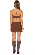 Rear view of a brown ribbed halter neck mini dress with a tie-back and delicate gold chain detail around the waist
