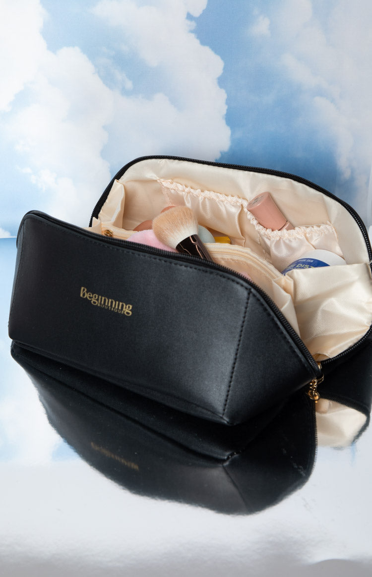 Open black cosmetic bag with light beige satin lining, featuring an internal zippered pocket and elasticated side compartments