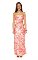 Our model wearing a  long satin-like maxi-skirt in a pink and yellow floral print featuring a high side slit and a flowing silhouette.