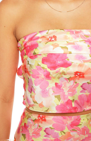 A close-up of a strapless crop top in a pink coral and yellow floral print on a satin-like fabric showing a gathered or folded detail across the bust.