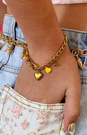 A close-up of a gold-toned chunky chain bracelet with a large puffed heart charm and a smaller flat heart charm.