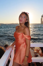 Side view of an orange satin off-the-shoulder mini dress with a draped neckline and flowy skirt