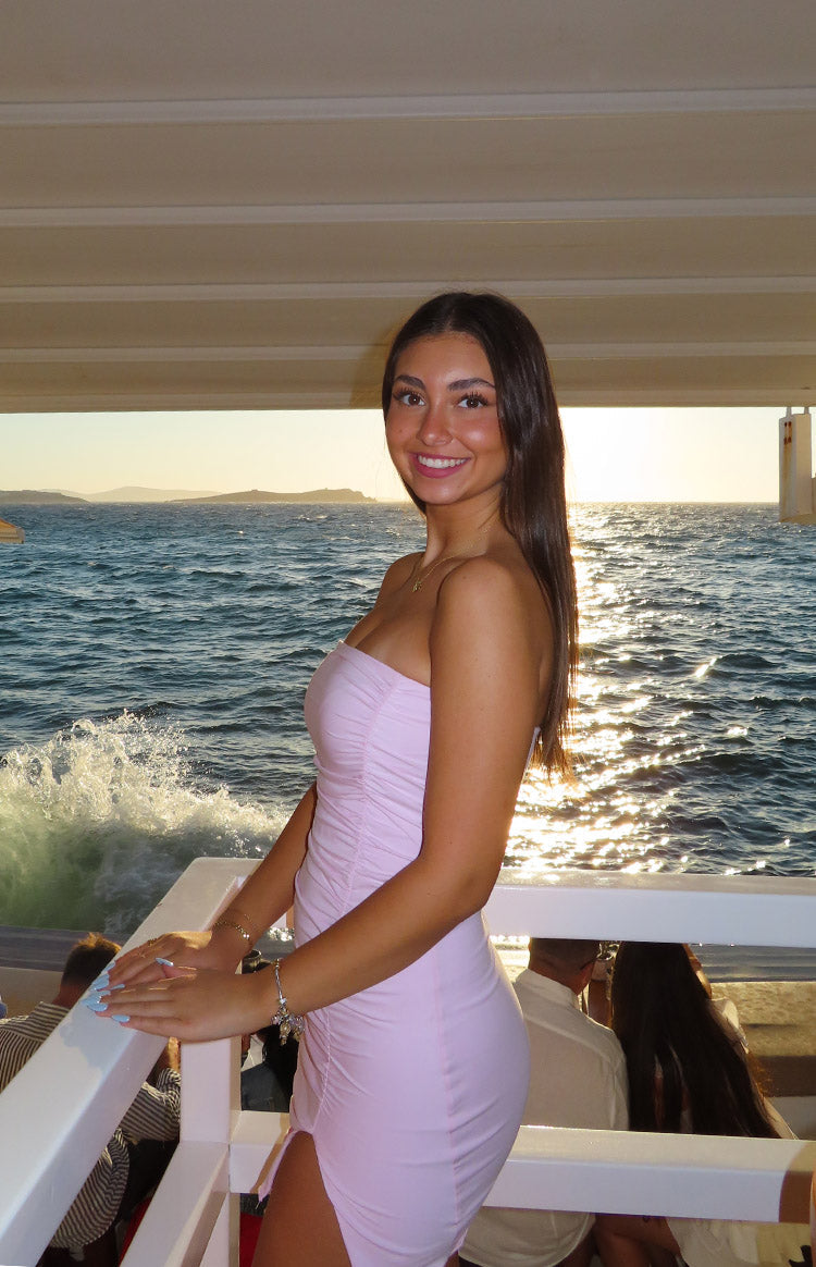 Side view of a baby pink strapless bodycon mini dress with full side ruching and a high slit