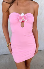 A close-up of a pink strapless bodycon mini-dress- featuring a ruched bustline with a keyhole detail and a large pink orchid embellishment at the center.