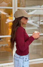 Side view of a fitted burgundy knit sweater with a white star graphic on the side, long ribbed sleeves, and a ribbed hem
