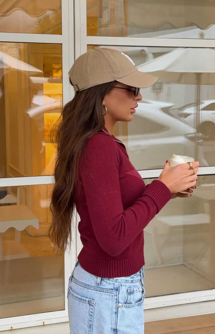 Side view of a fitted burgundy knit sweater with a white star graphic on the side, long ribbed sleeves, and a ribbed hem