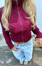 Burgundy knit sweater with a subtle knit star pattern, full zip front, high mock neck, and ribbed cuffs