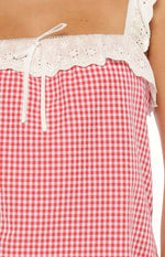 Close-up of the red gingham mini dress with white eyelet lace trim, front tie, and ruffled lace strap