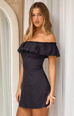 Side view of a fitted black polka dot mini dress featuring a wide elasticated ruffled off-shoulder neckline