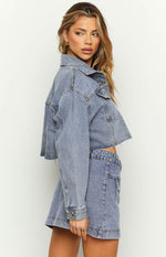 Side view of the mid wash denim cropped jacket with a raw frayed hem and buttoned cuffs