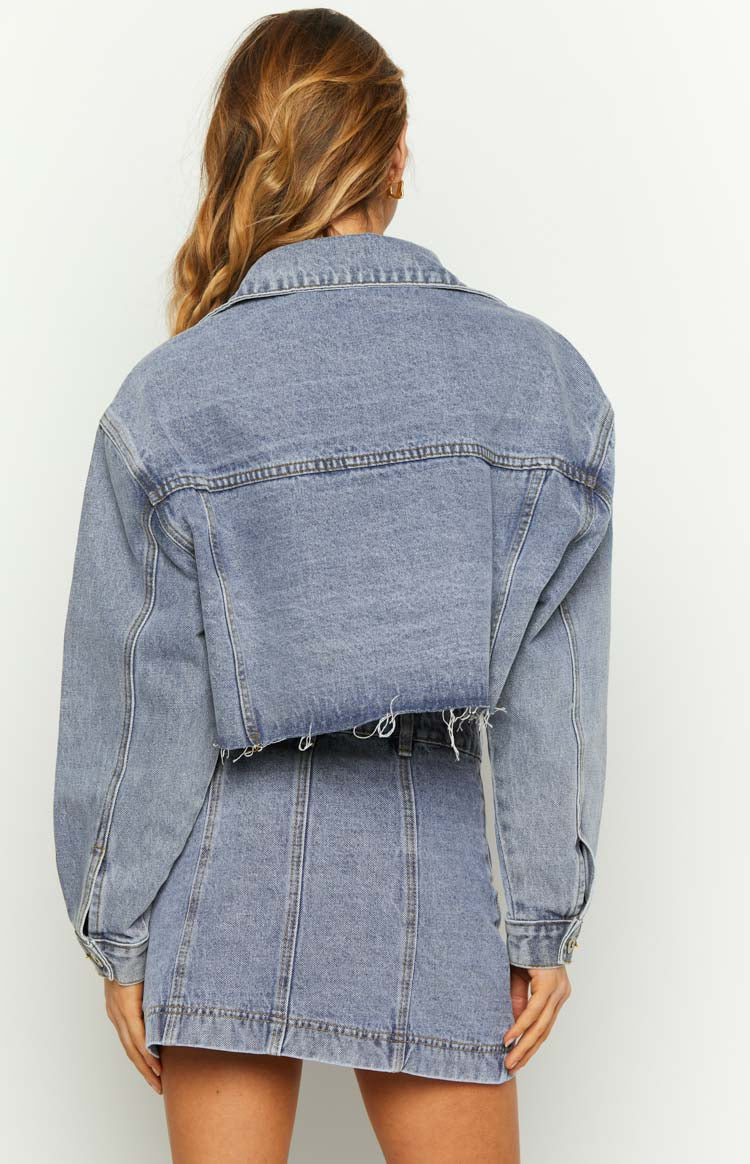Back view of a mid wash denim cropped jacket with a raw frayed hem and classic stitching details