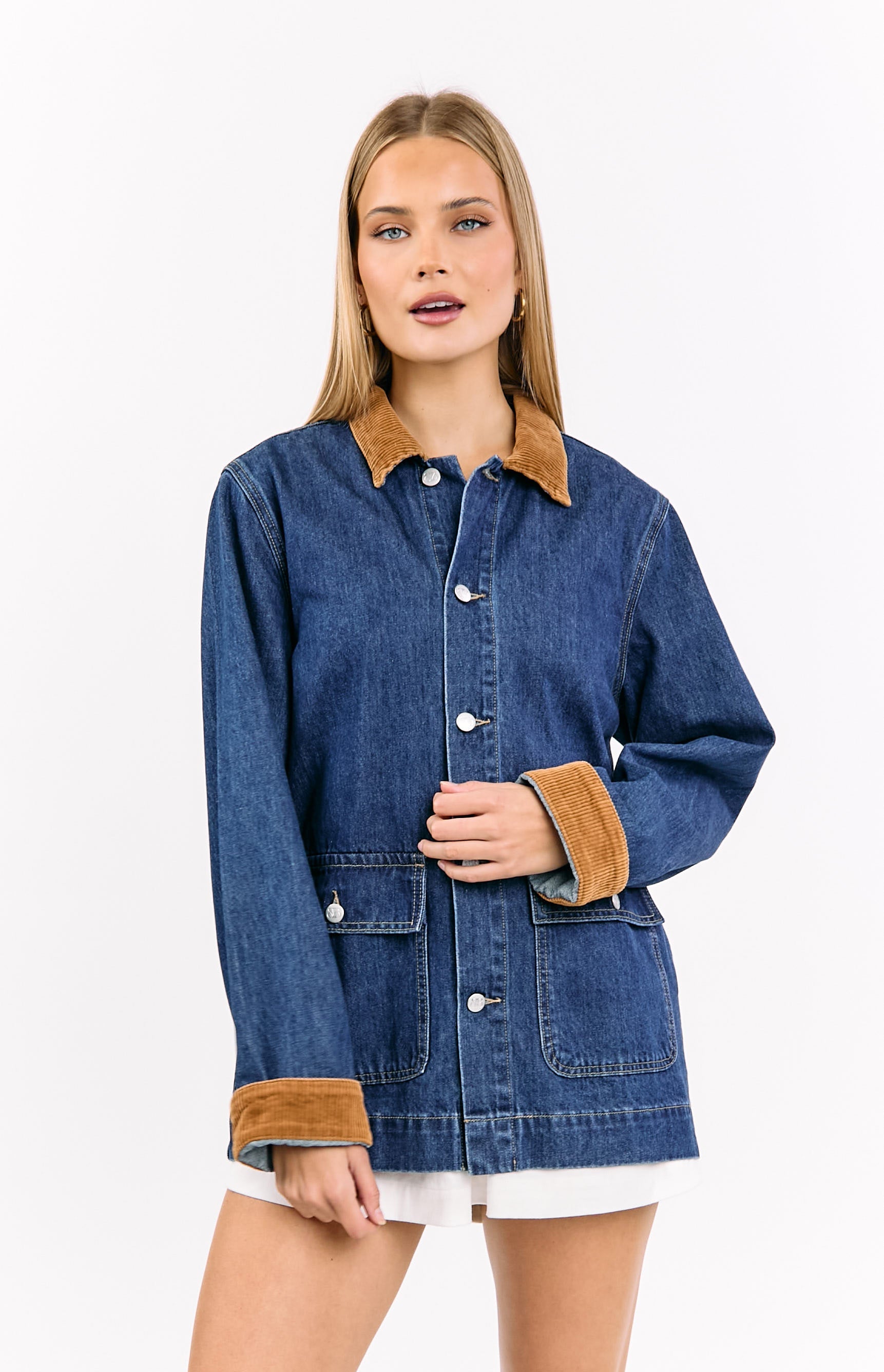 Front view of a mid wash denim oversized jacket featuring a tan corduroy collar, white buttons, and rolled corduroy cuffs