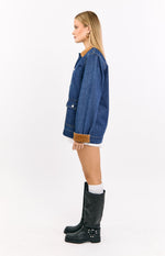Side view of the mid wash denim oversized jacket with a tan corduroy collar, patch pocket, and rolled cuffs