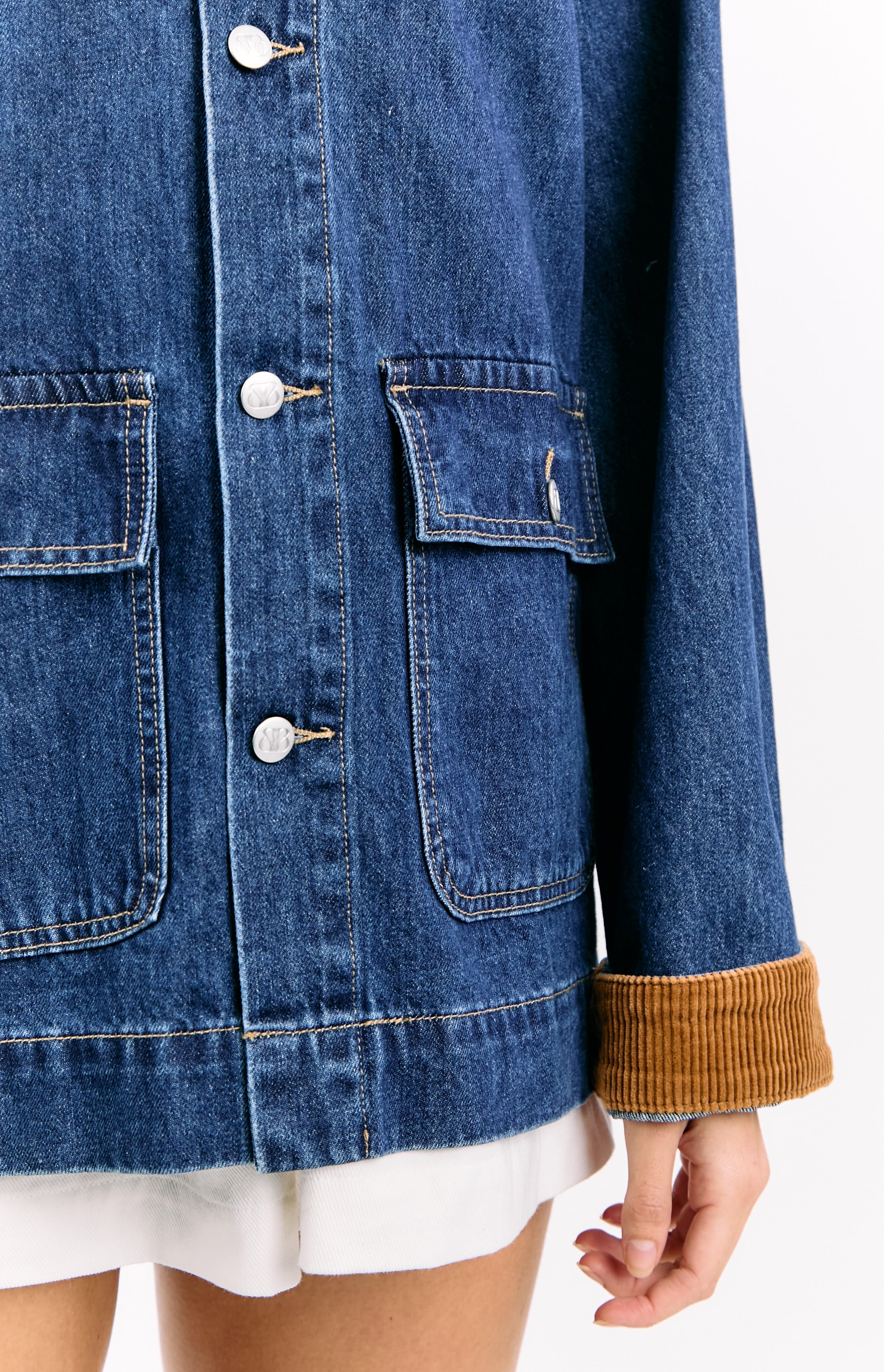 Front detail of the mid-wash denim jacket with buttoned chest flap pockets and rolled brown corduroy cuffs