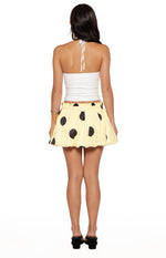 Back view of a yellow mini skirt with black polka dots, a shirred elastic waistband, and a bubble hem