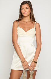Front view of a cream mini dress with a ruched sweetheart neckline and a smooth satin A-line skirt