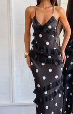 Close-up of the black polka dot maxi dress showing the V-neck, spaghetti straps, and diagonal ruffle tiers