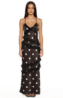 Model wearing a black polka dot maxi dress with ruffled layers and spaghetti straps for a wedding guest